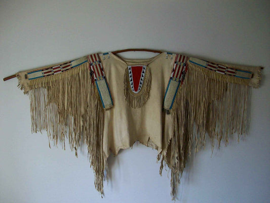 Traditional Native American garment with fringes and beadwork on a white wall
