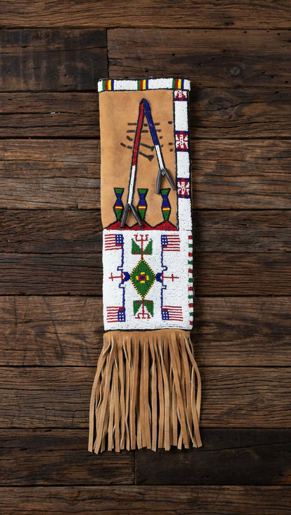 A Native American style beaded fringed belt or sash laid flat on a dark rustic wooden background. The belt features a tan leather base, white beaded panels with geometric patterns, and colorful beadwork in red, blue, green, and yellow.
