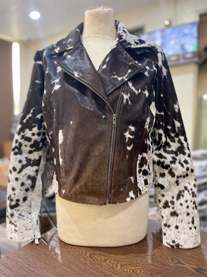 A cowhide jacket displayed on a mannequin, featuring a mix of black and white spots on the sleeves and a solid brown body with a zipper.