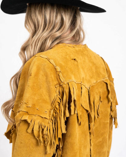 A close-up back view of a person wearing a distressed mustard yellow suede fringe jacket and a black wide-brim hat, against a plain white background.