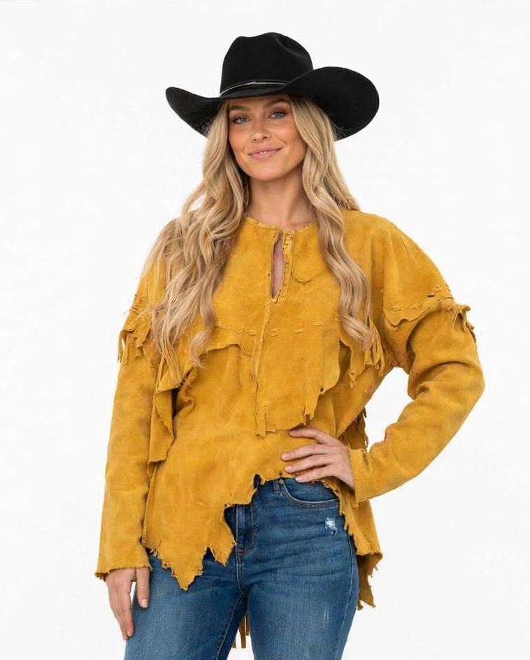 A woman modeling a mustard yellow suede fringe top with a split neckline and a black cowboy hat, paired with blue jeans, against a plain white background.