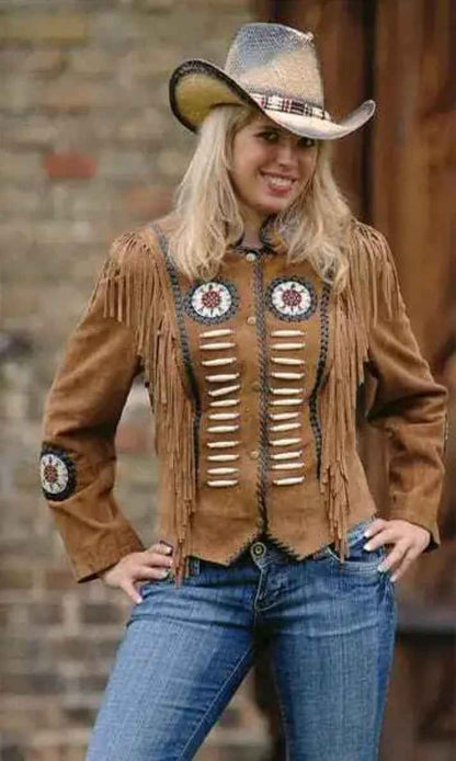 Woman wearing a brown suede jacket with fringe and decorative elements, standing against a brick wall.