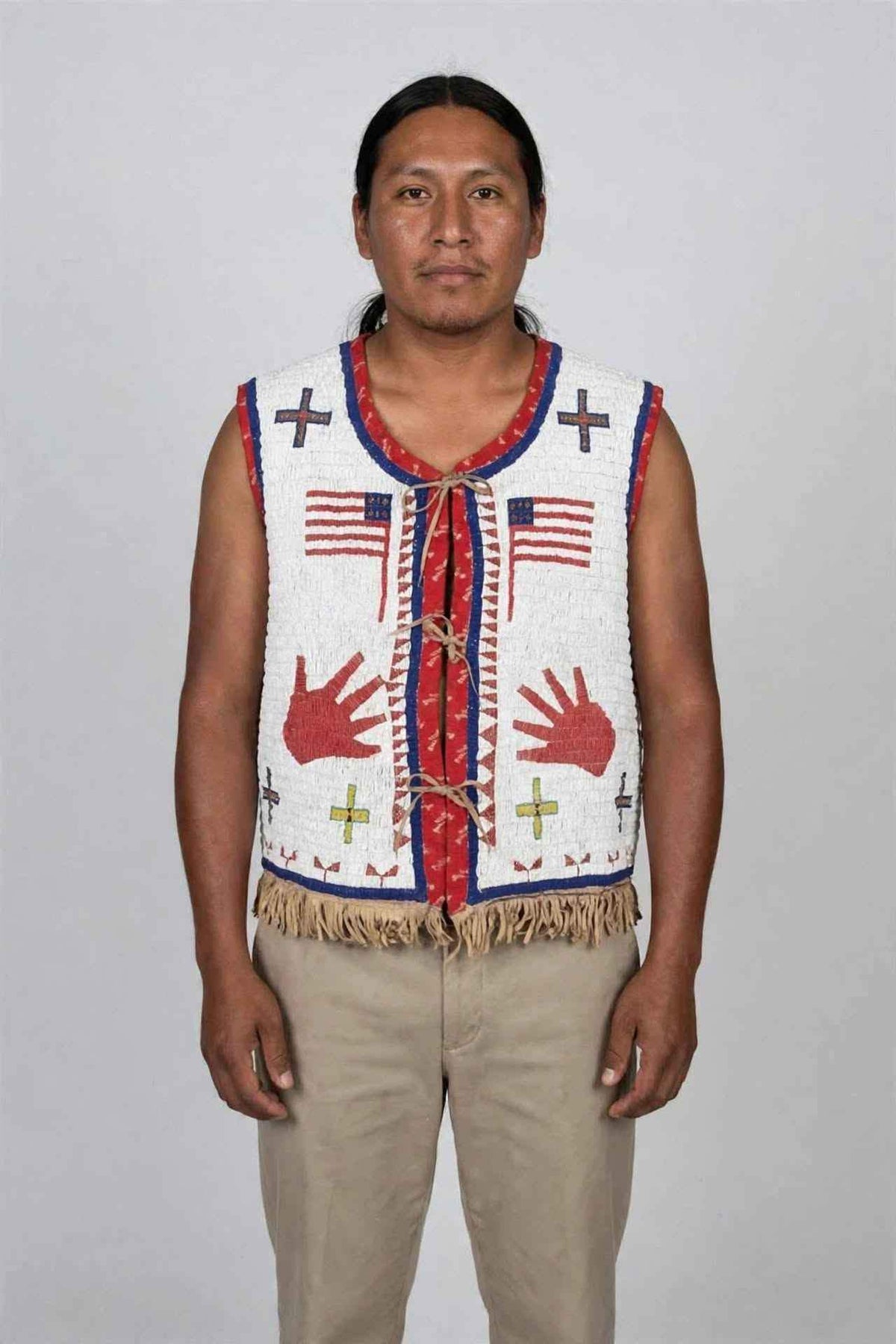 Man wearing a white beaded fringe vest with tribal patterns and American flag motifs.