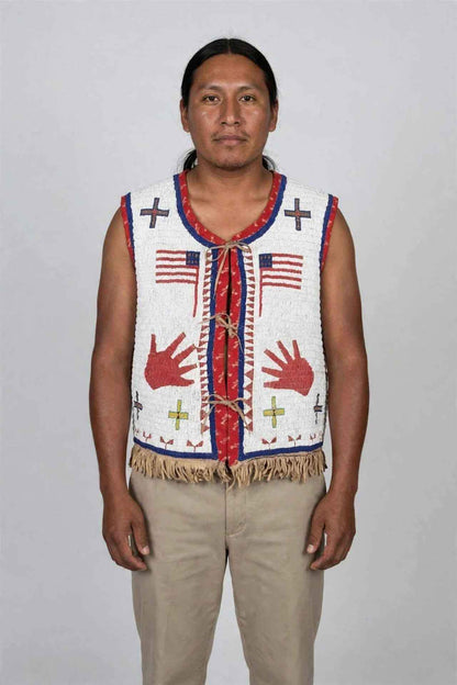 Man wearing a white beaded fringe vest with tribal patterns and American flag motifs.